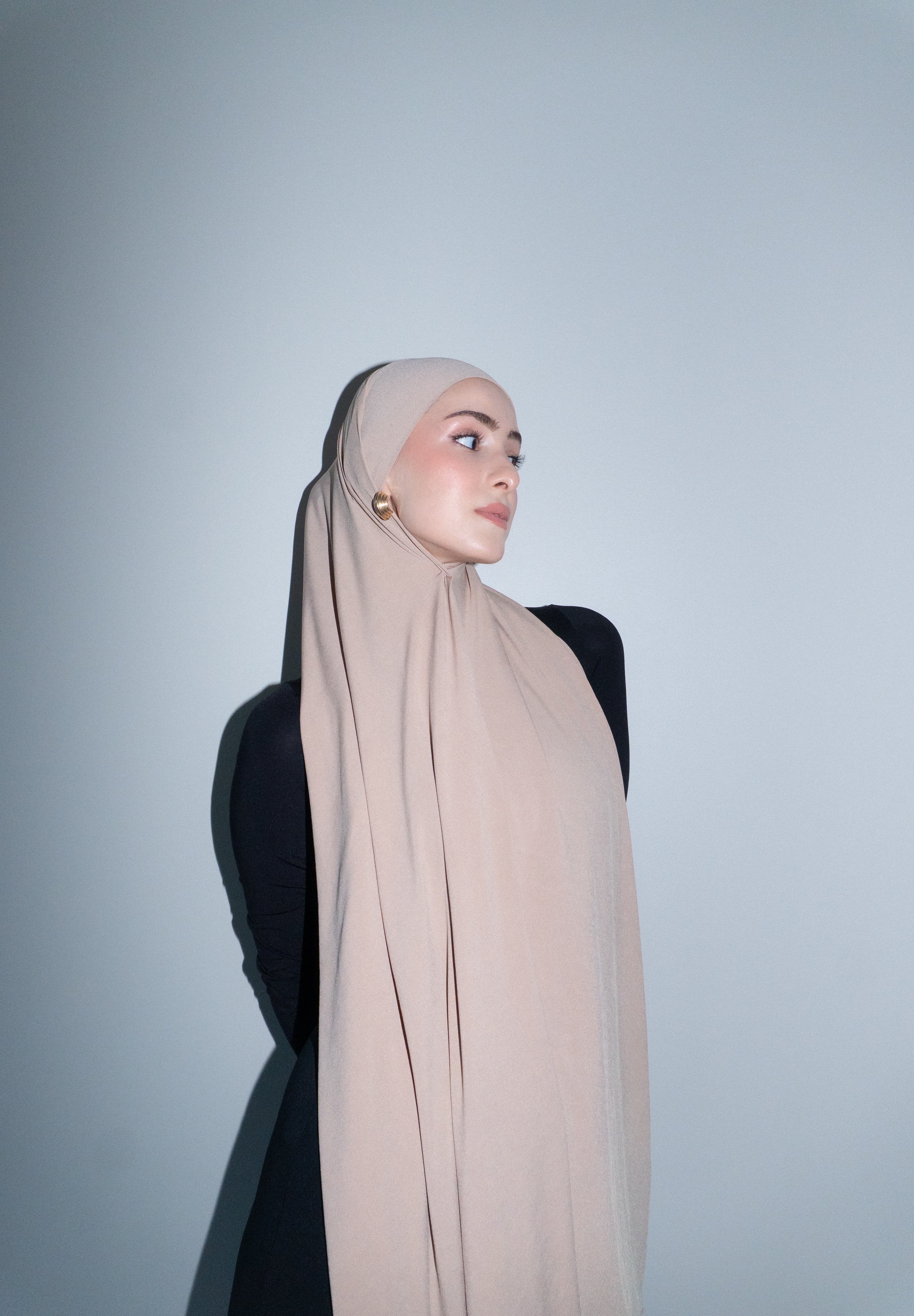 Woman wearing a beige hijab against a plain background