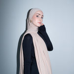 Woman wearing a beige hijab against a light gray background