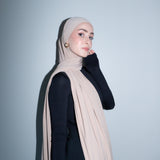 Woman wearing a beige hijab against a light gray background