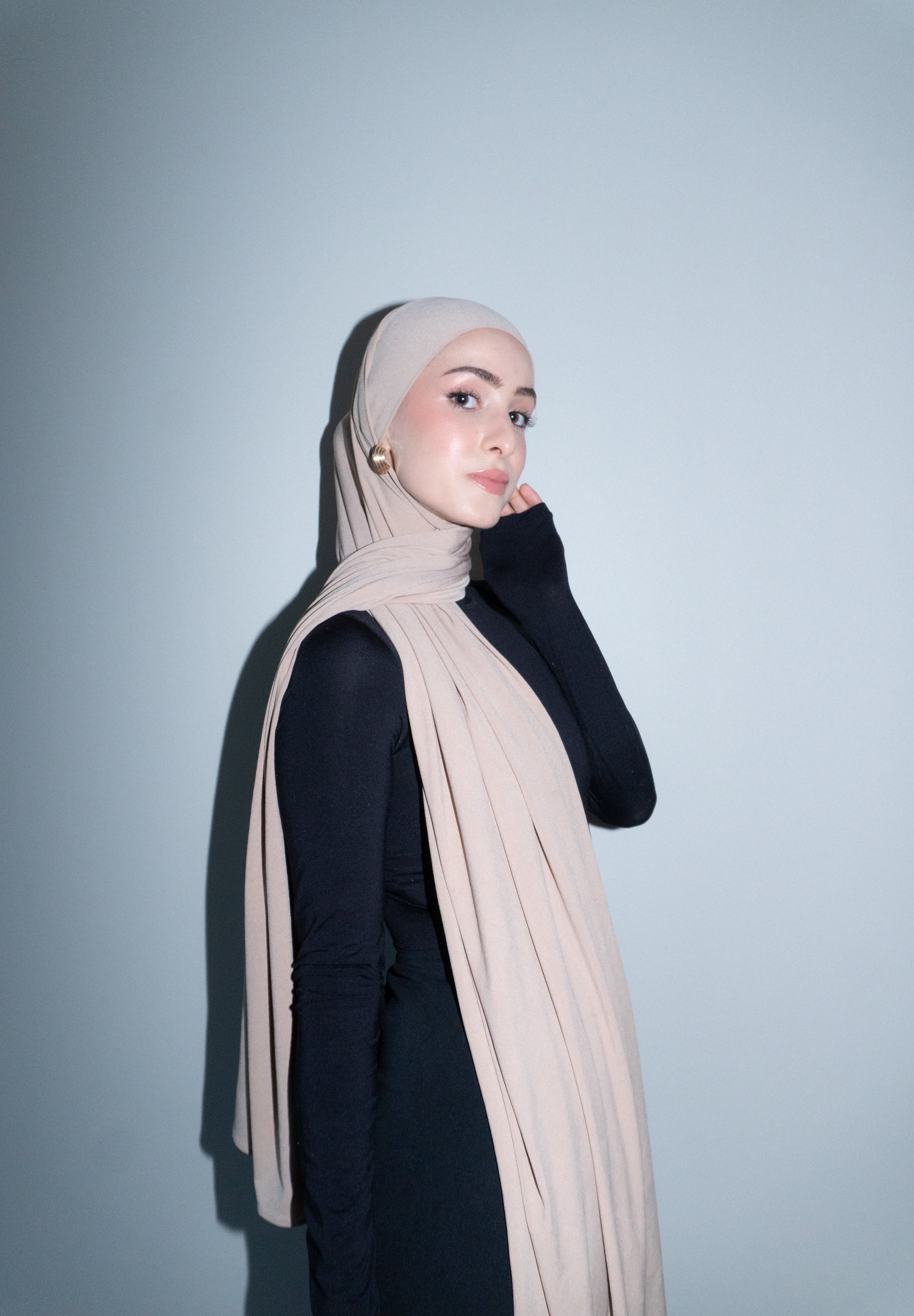 Woman wearing a beige hijab against a light gray background