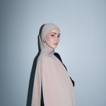 Woman wearing a beige hijab against a light gray background