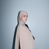 Woman wearing a beige hijab against a light gray background