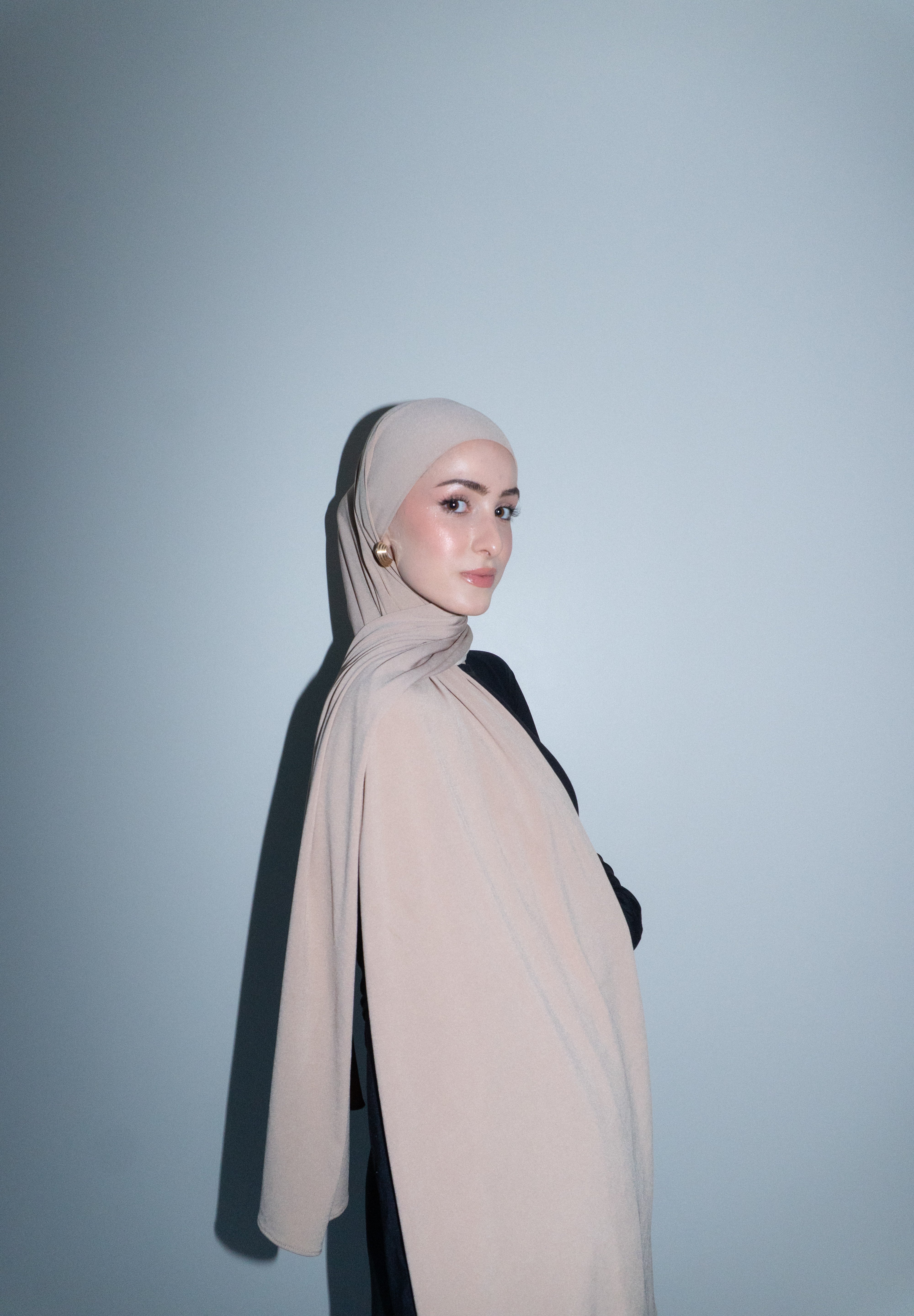 Woman wearing a beige hijab against a light gray background